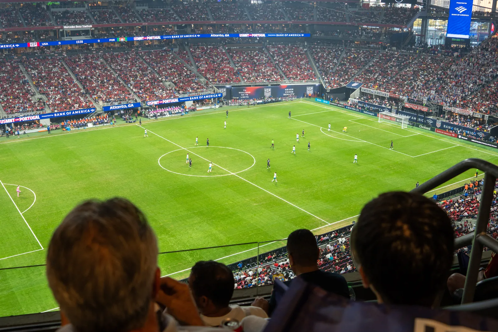 A football match seen from a stadium suite, spectators in the foreground